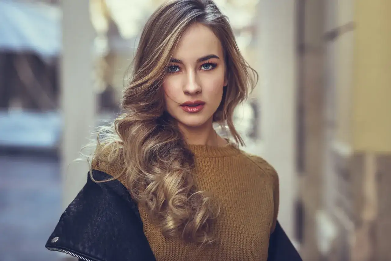 Młoda kobieta z burzą blond loków, w skórzanej kurtce i swetrze, inspiruje do tego, jak zostać modelką.
